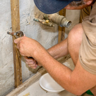 Plumber using channel-lock pliers to attach a nut to a water pipe. He has a bowl beneath to catch any remaining water.   Authentic and accurate content depiction.
